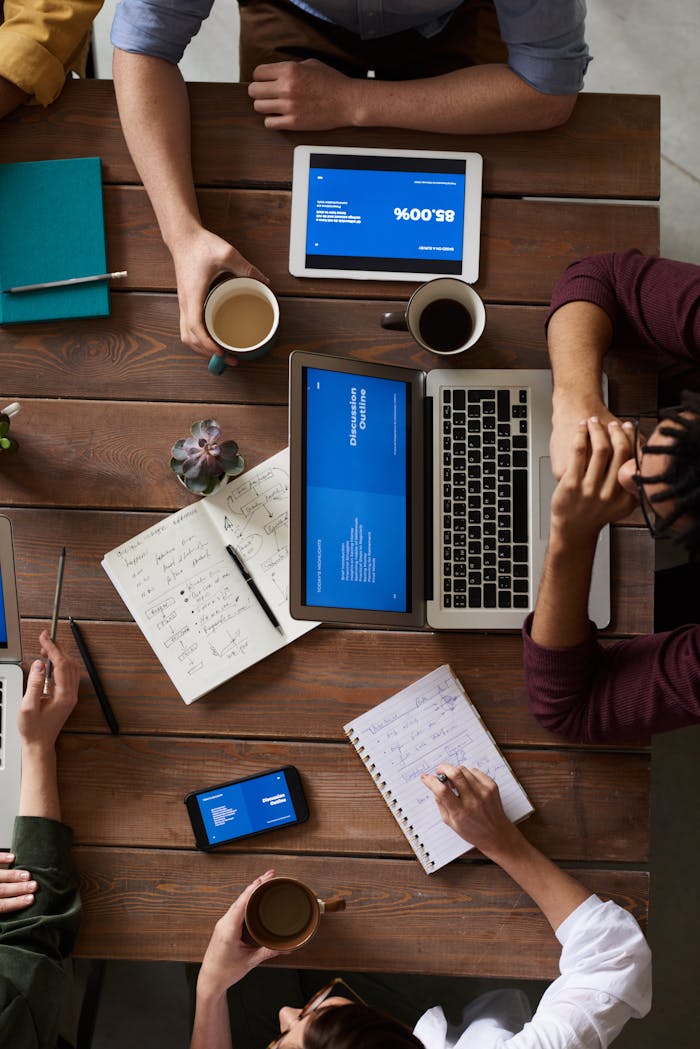 Group of coworkers discussing business strategies with laptops and tablets in a modern office setting. www.max-it-development.com